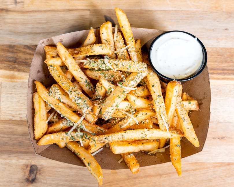 Golden french fries seasoned with herbs and parmesan cheese, served with a side of creamy white dipping sauce.