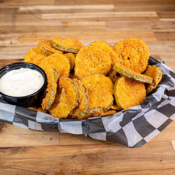Fried pickles with ranch dipping sauce in a checkered paper basket
