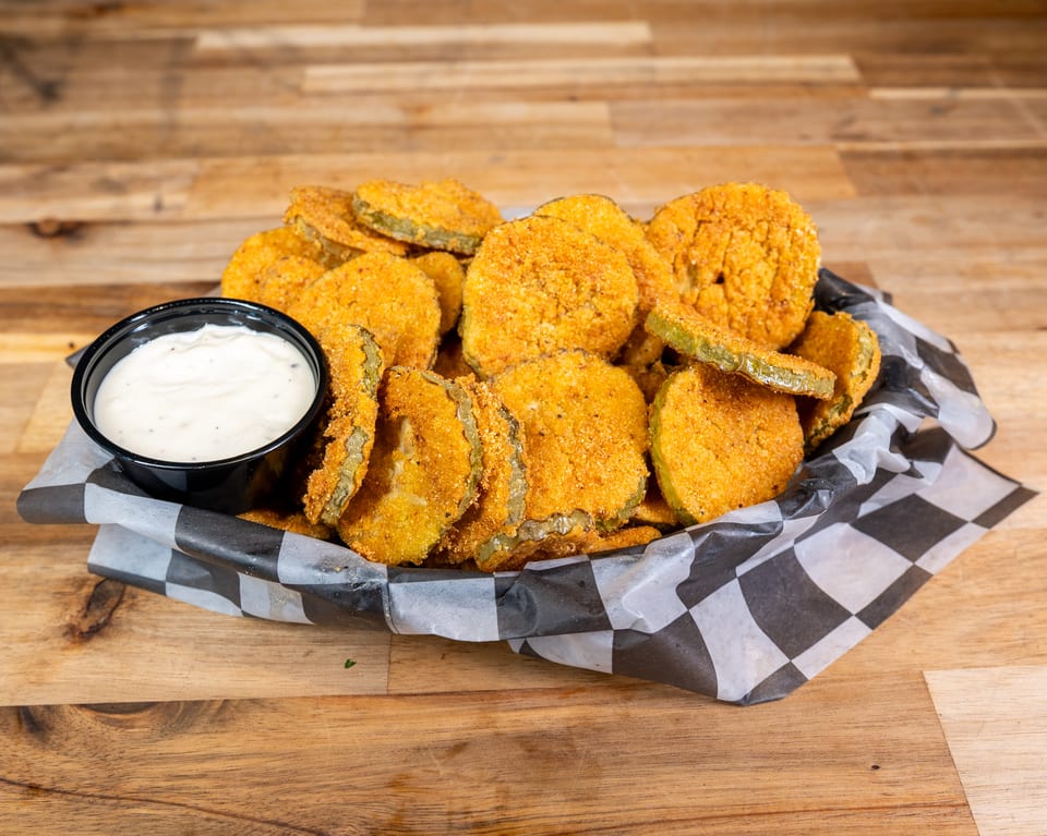 Fried pickles with ranch dipping sauce in a checkered paper basket