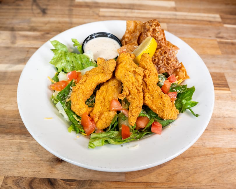 Crispy fried chicken tenders on a bed of fresh green salad with tomatoes, cheese, and dressing.