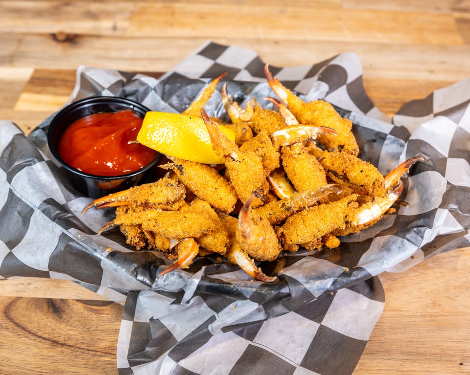 Fried crab fingers with cocktail sauce and lemon in a checkered paper basket