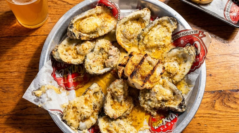 Chargrilled oysters with garlic butter on a metal tray with a beer