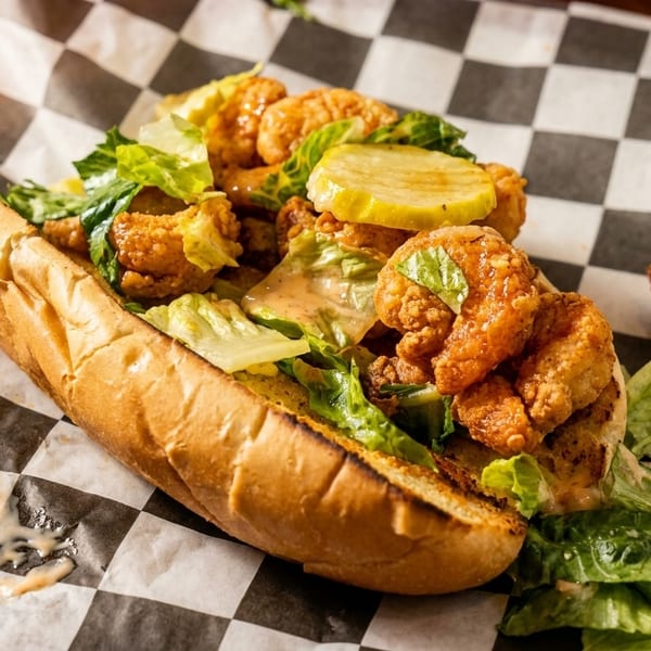 Fried shrimp po'boy with lettuce, pickles, and remoulade on checkered paper