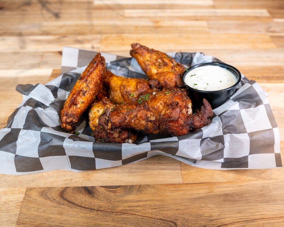 Crispy chicken wings with ranch dipping sauce in a checkered paper basket