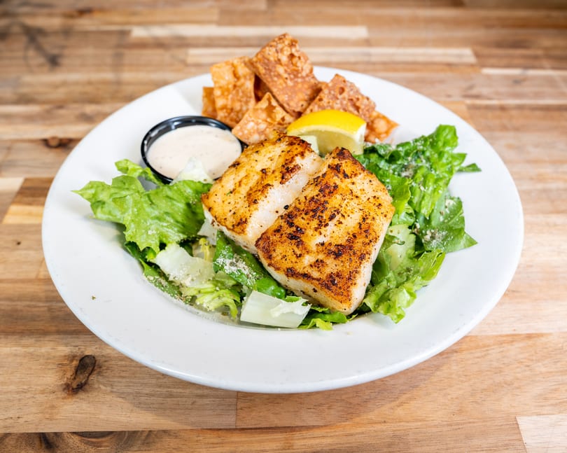 Grilled fish fillets on a bed of green salad with dressing, lemon, and crispy wontons.